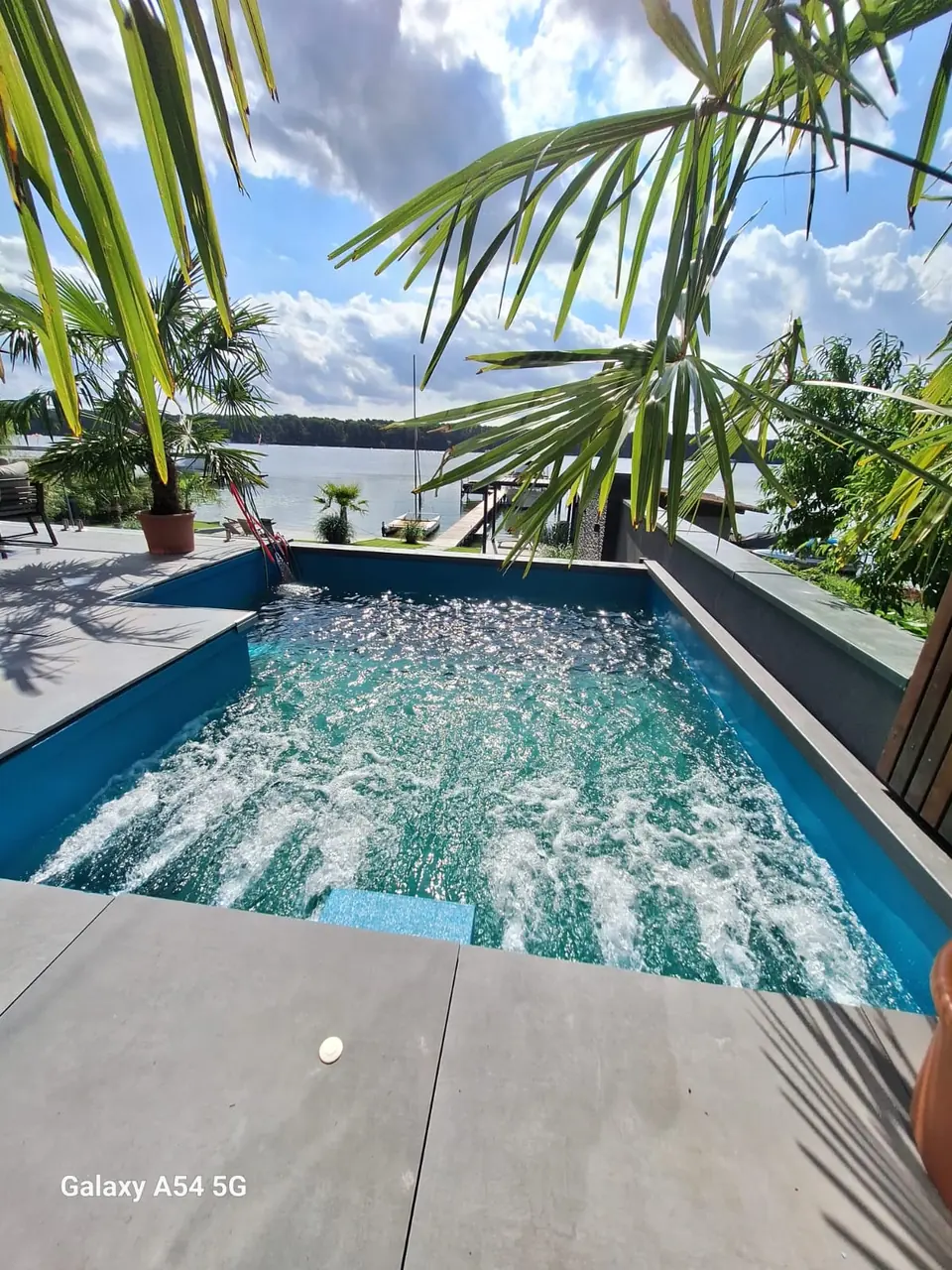 Blick unter Palmen auf die bewegte Wasserfläche – No1Pool